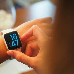 An individual operating a digital smartwatch displaying time with a blue interface.