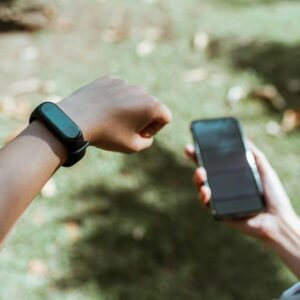 An individual checking both a smartwatch and smartphone outdoors with a blurred grass background.
