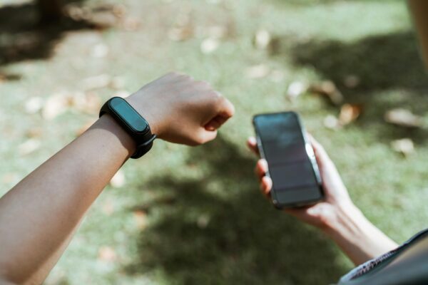An individual checking both a smartwatch and smartphone outdoors with a blurred grass background.