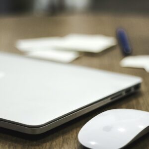 A clean and minimalist workspace featuring a closed laptop and wireless mouse on a wooden desk.