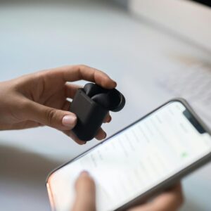 Close-up view of hands connecting wireless earbuds to a smartphone, emphasizing modern technology.